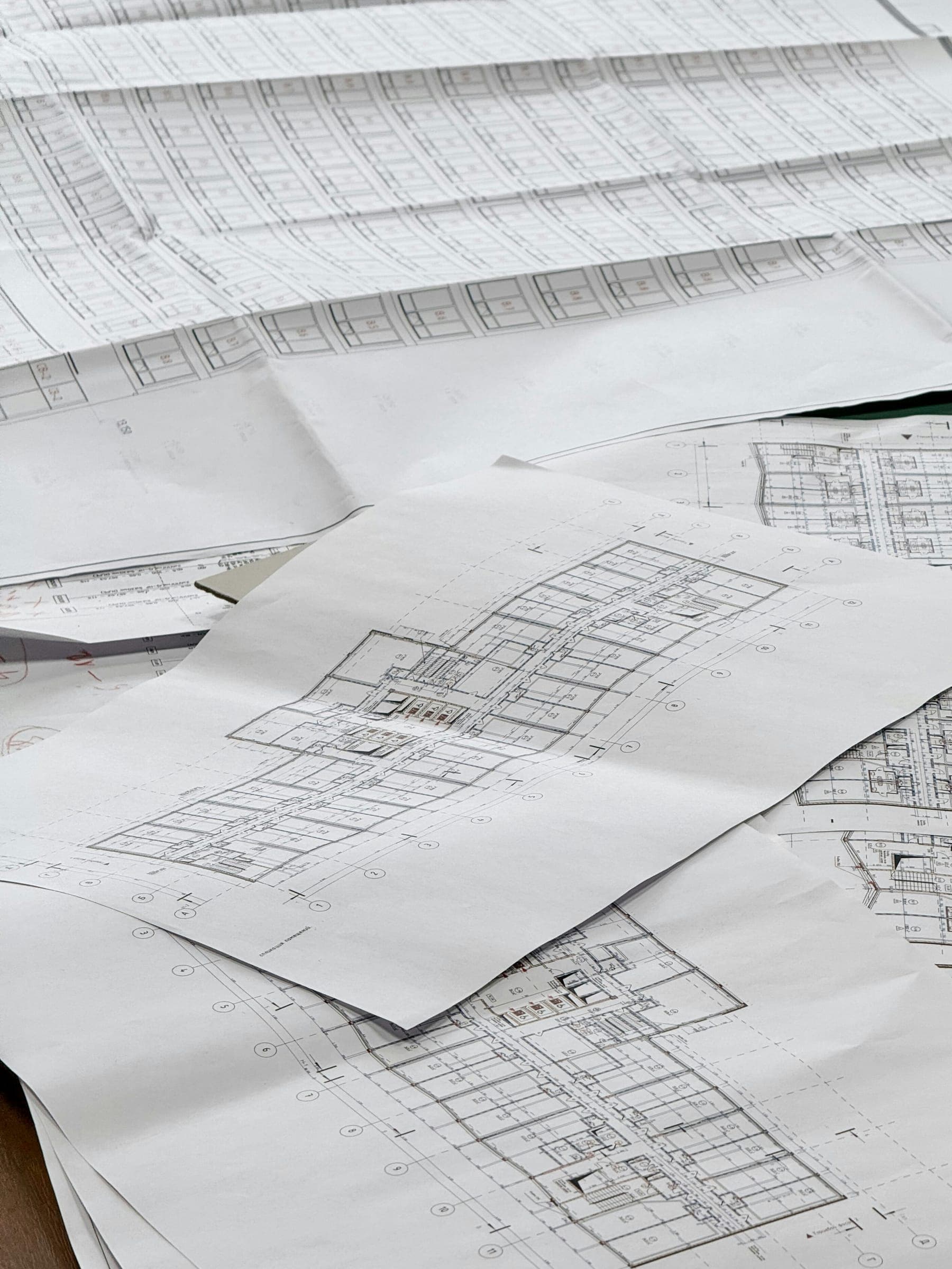Udprintede plantegninger og facadetegninger til et etagebyggeri spredt ud på et bord